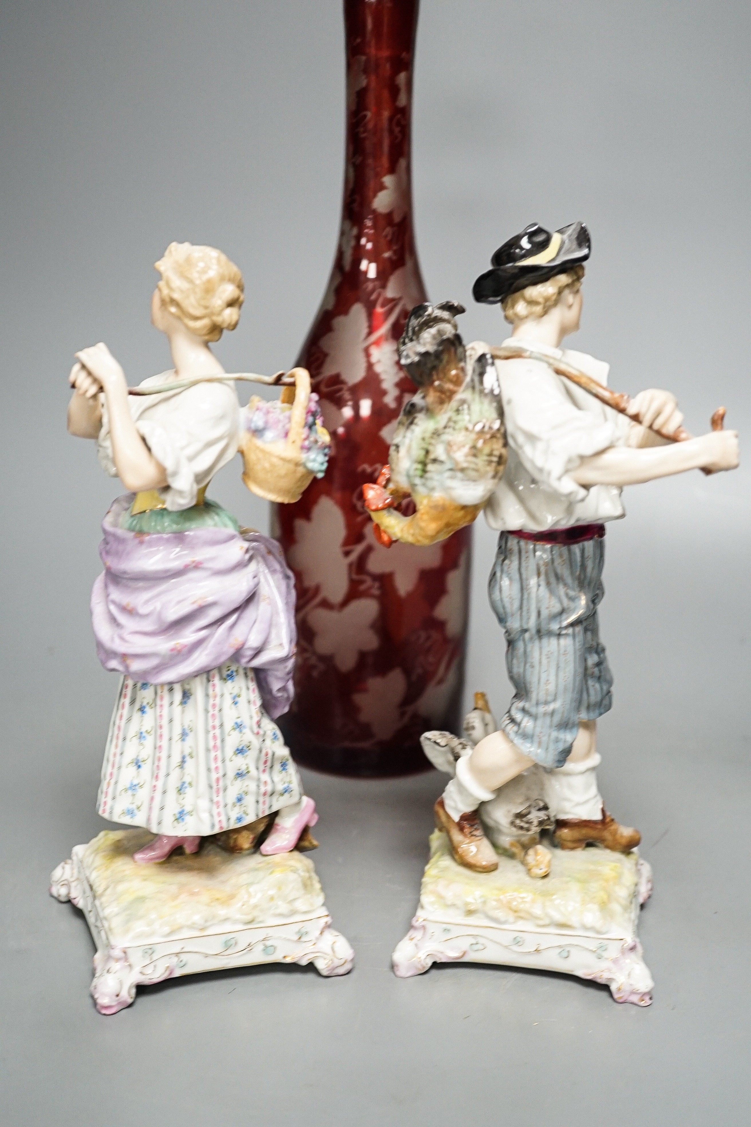 A late 19th century Bohemian wheel engraved ruby glass decanter and a pair of continental porcelain figures, decanter 37 cms high, including stopper.